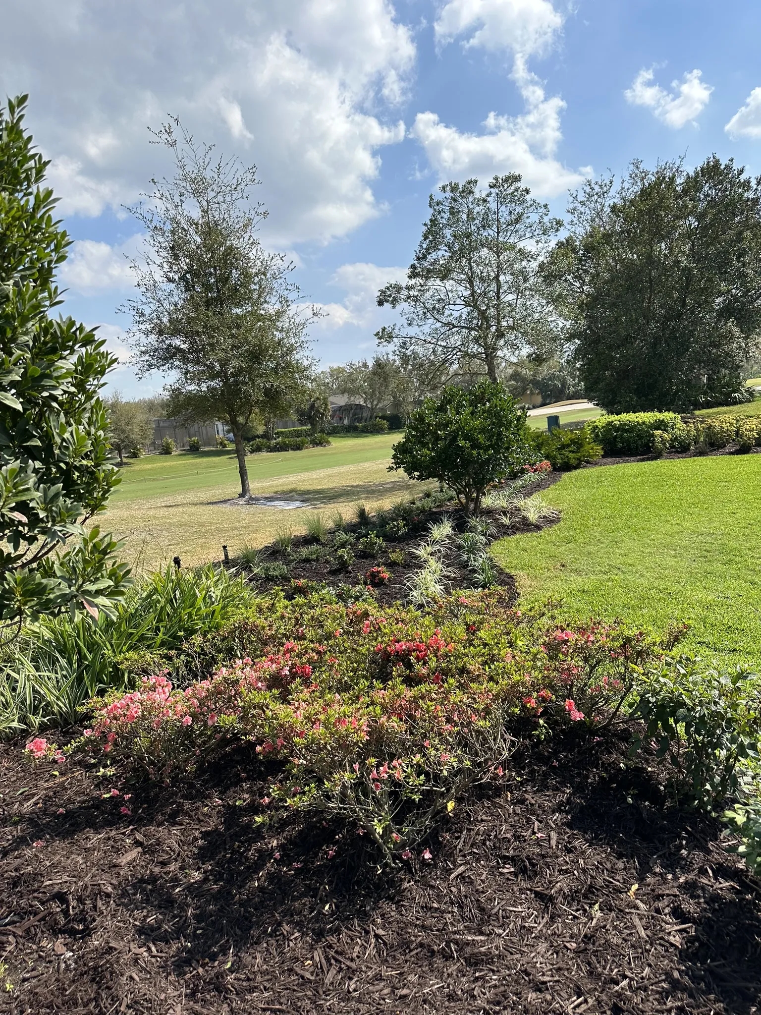 A sprinkler system waters a lush green lawn and colorful flower beds on a sunny day.